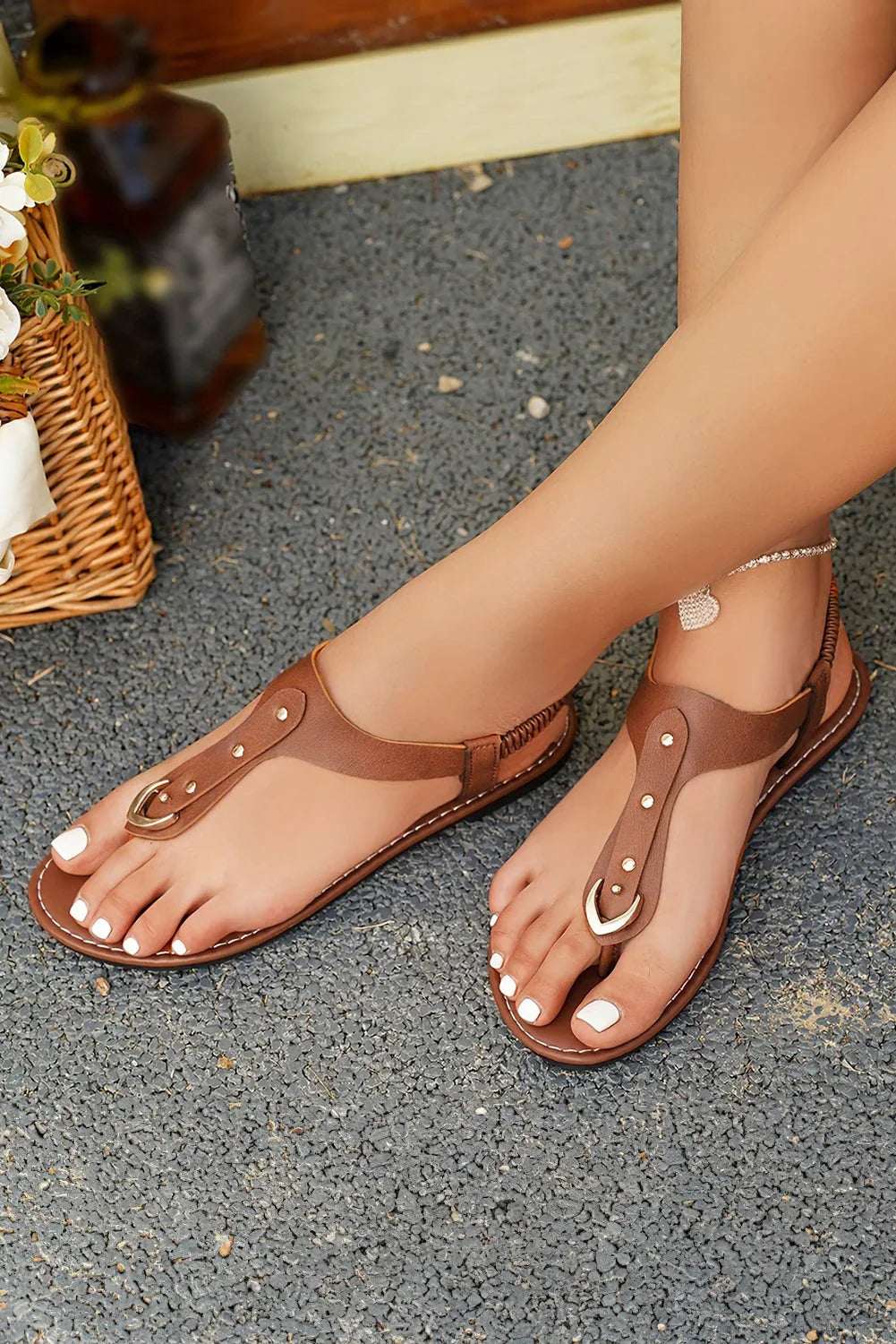 Woman wearing brown leather flat sandals with gold-tone accents on textured pavement