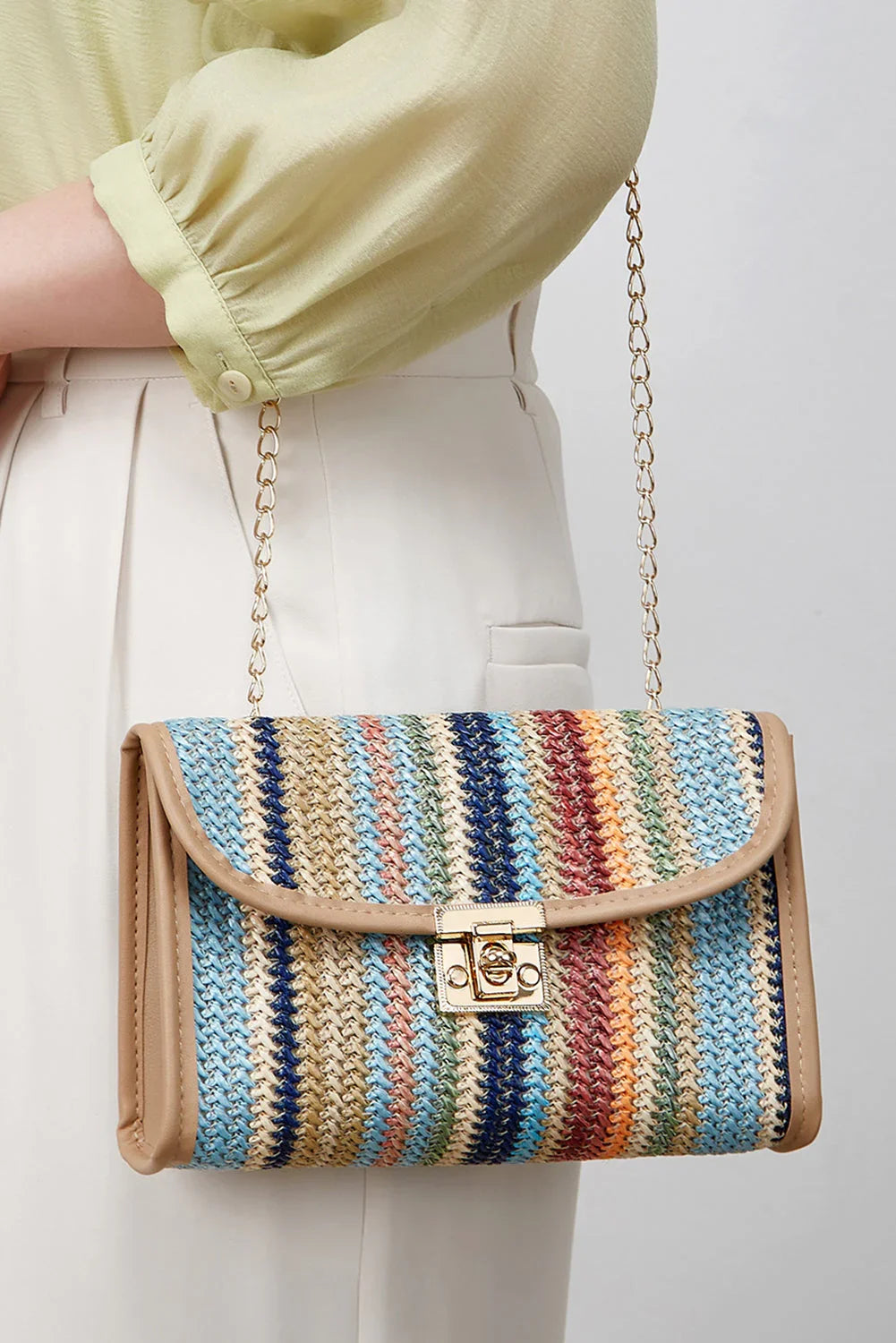 Woman holding a striped woven crossbody bag with gold chain strap and clasp closure