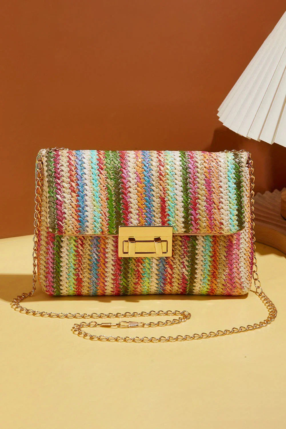 Colorful woven crossbody bag with gold chain strap and clasp on a neutral background.