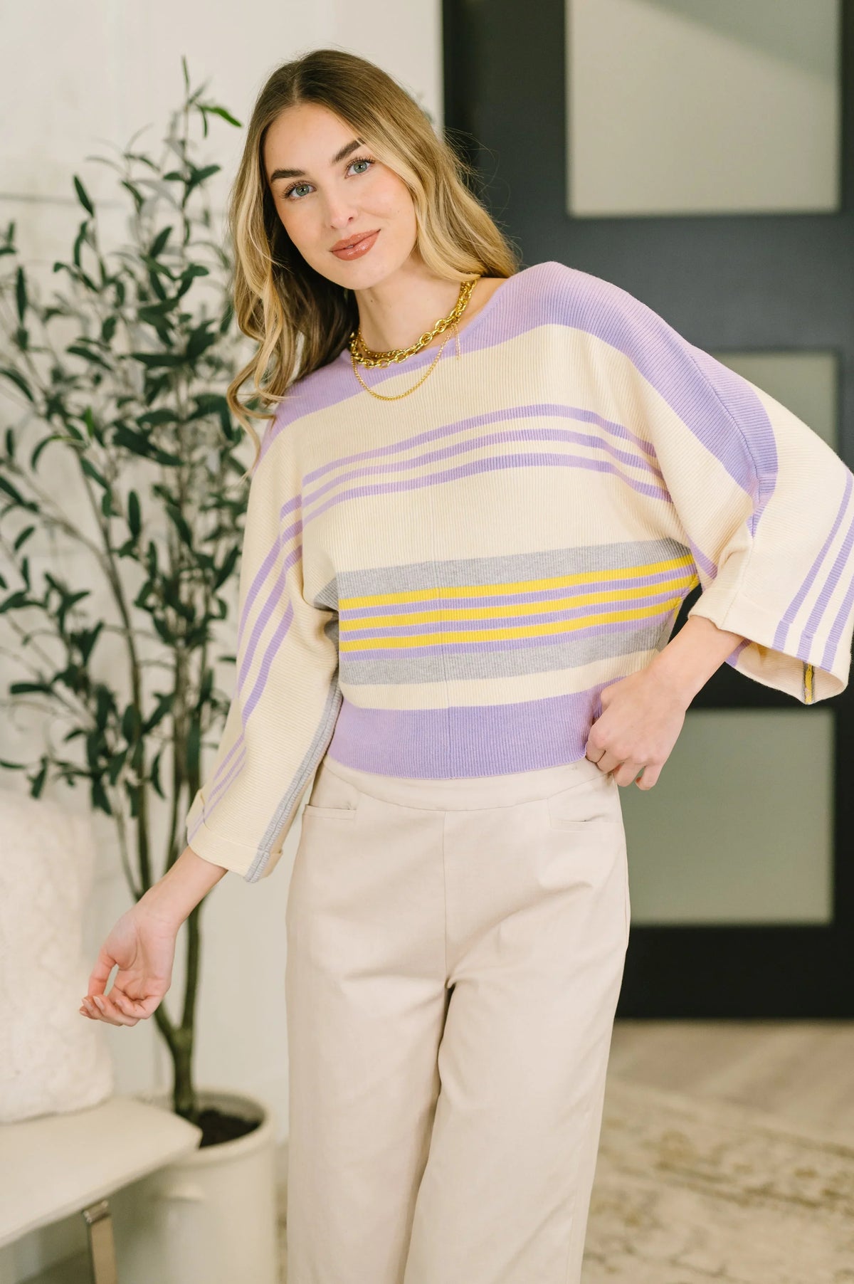 Woman wearing a pastel striped dolman sleeve top with cream wide-leg pants indoors.