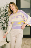Woman wearing a pastel striped dolman sleeve top with cream wide-leg pants indoors.