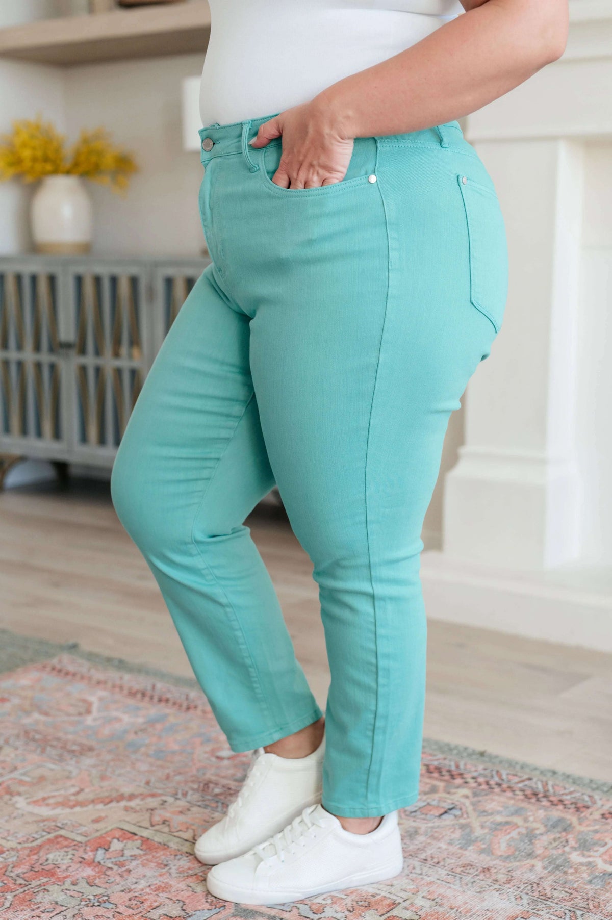 Woman wearing high rise aquamarine slim jeans and white sneakers in a modern living room