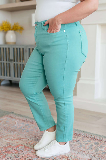 Woman wearing high rise aquamarine slim jeans and white sneakers in a modern living room