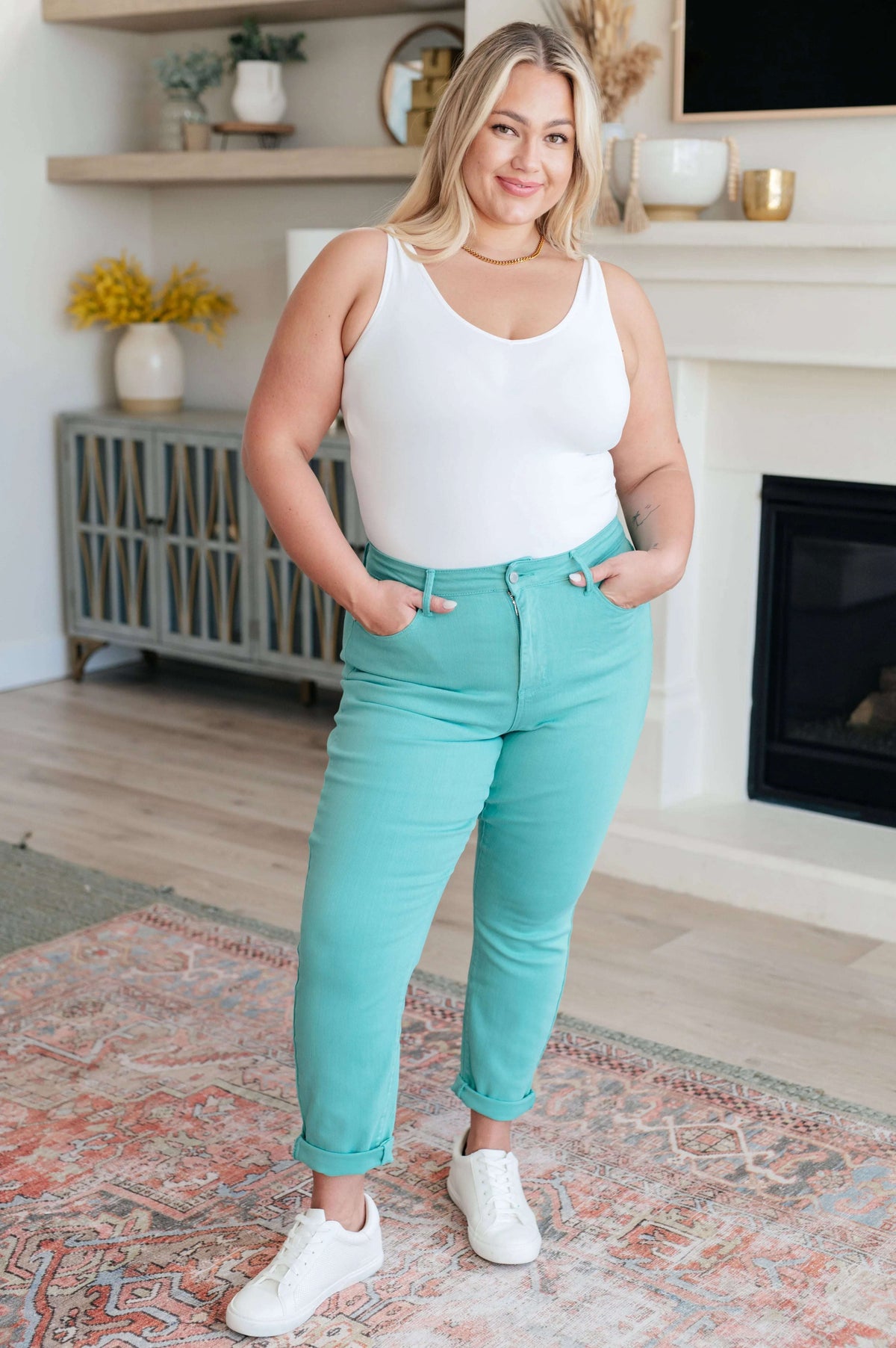 Woman modeling high rise aquamarine slim jeans and white tank top in a modern living room