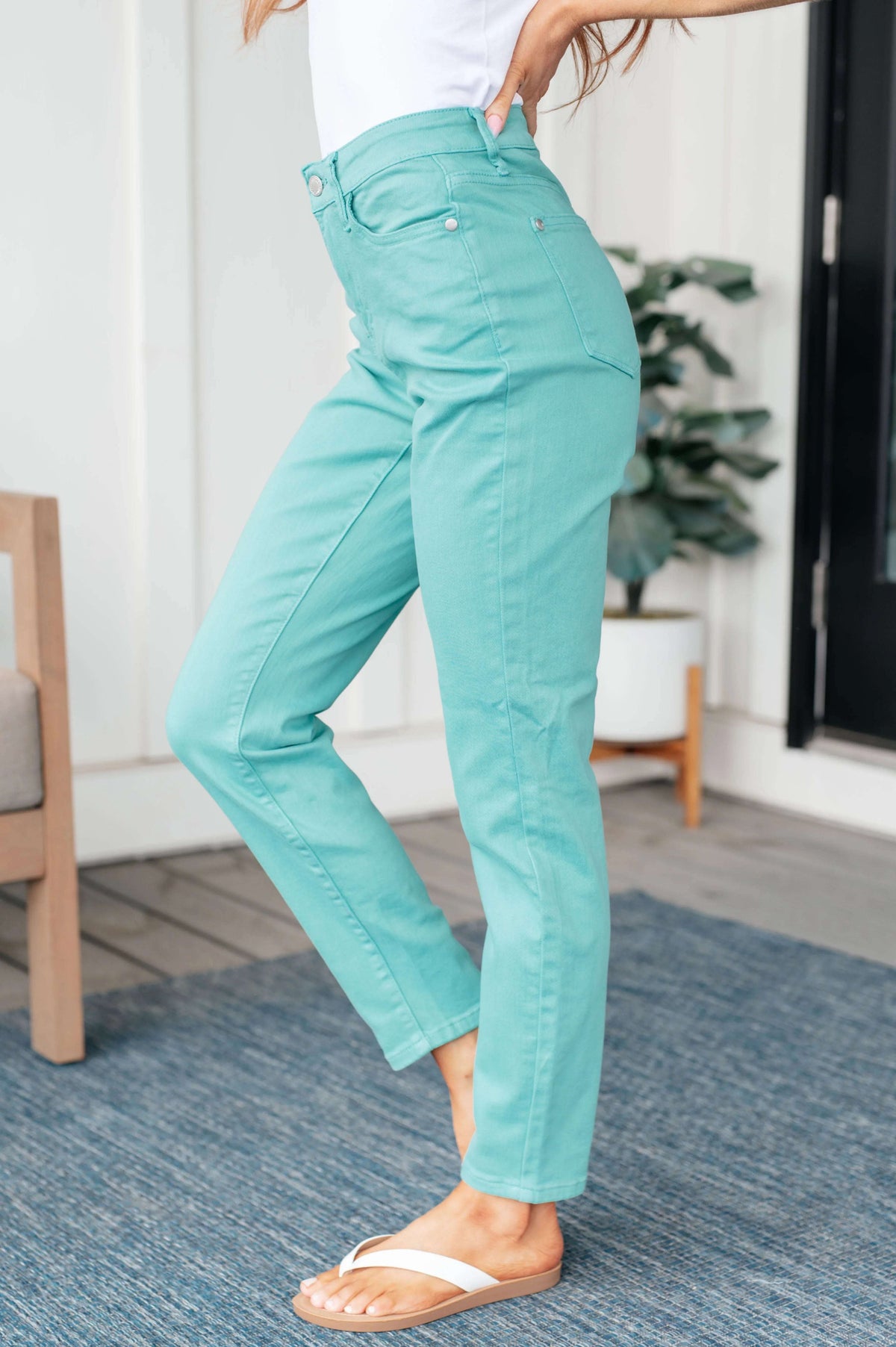 Woman wearing aquamarine high-rise slim jeans, white top, and sandals on a porch