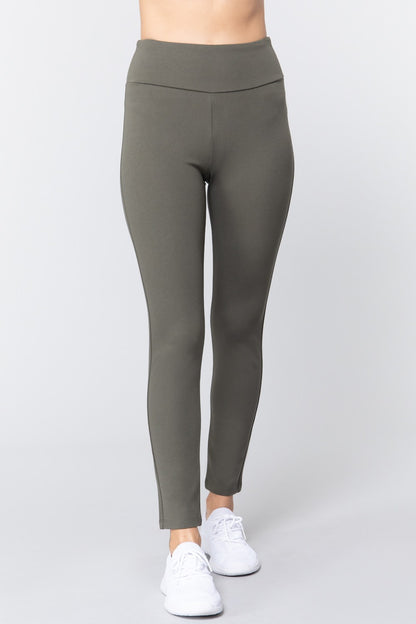 Woman wearing olive green waist band long ponte pants with white sneakers on a white studio background.