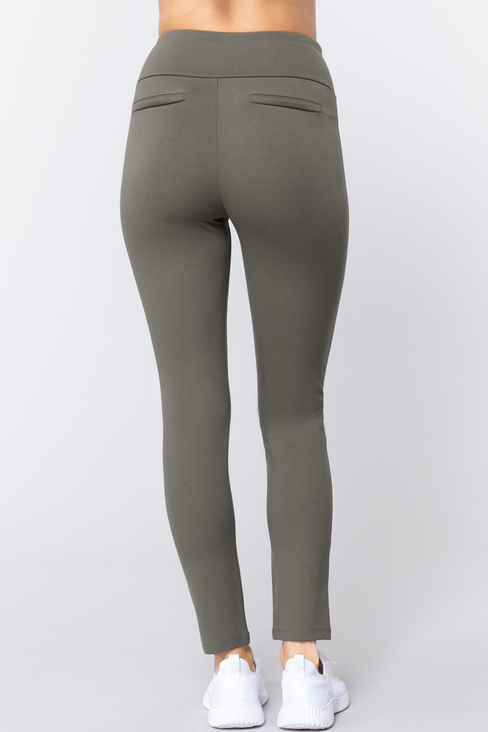 Woman wearing olive green waist band long ponte pants with back slit pockets with white sneakers on a white studio background