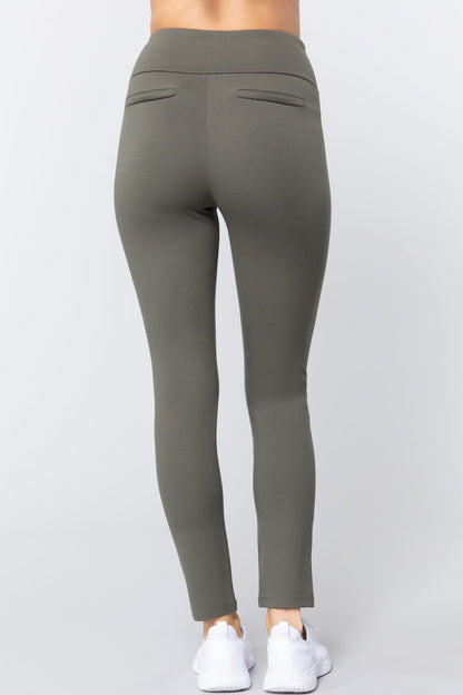 Woman wearing olive green waist band long ponte pants with back slit pockets with white sneakers on a white studio background