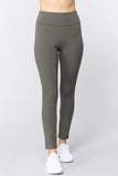 Woman wearing olive green waist band long ponte pants with white sneakers on a white studio background.