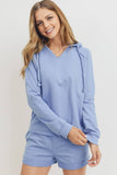 A woman modeling a light blue long-sleeve hooded sweatshirt and matching shorts set against a plain light background.