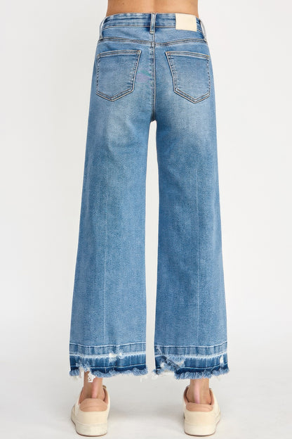 A woman wearing Tummy Control Cropped Wide Leg Jeans with a frayed hem and white sneakers against a white background.
