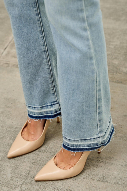 Light wash wide-leg jeans with raw hems paired with nude pointed-toe heels on concrete.