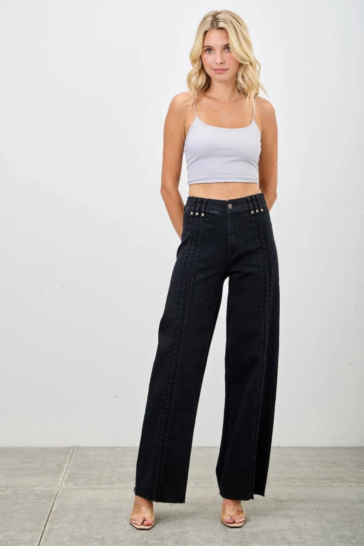 Woman in a white cropped tank top and high-waisted wide-leg black jeans standing indoors