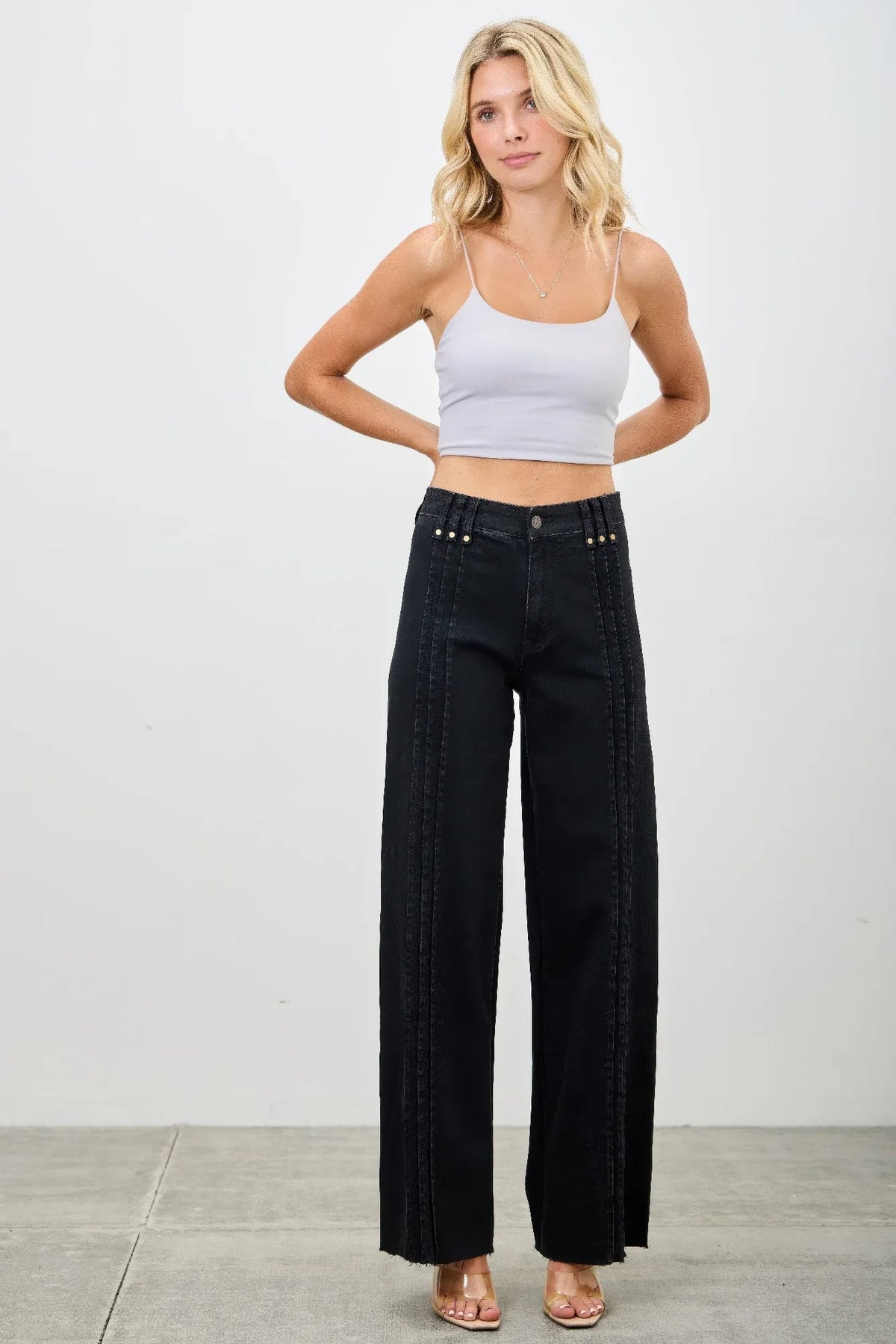 Woman in white cropped tank top and high-waisted black wide-leg pants with stud details