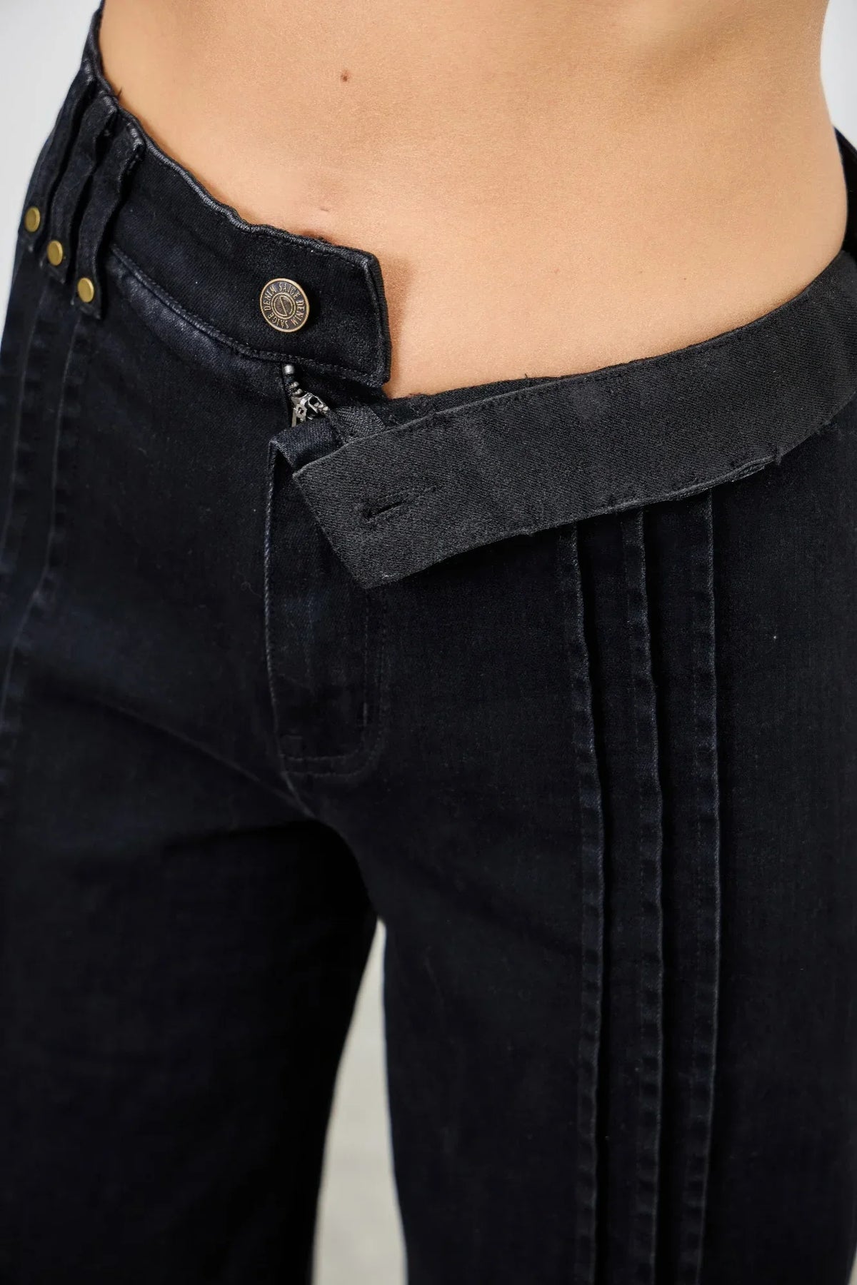 Close-up of black high-waisted jeans with double button and exposed waistband detail.