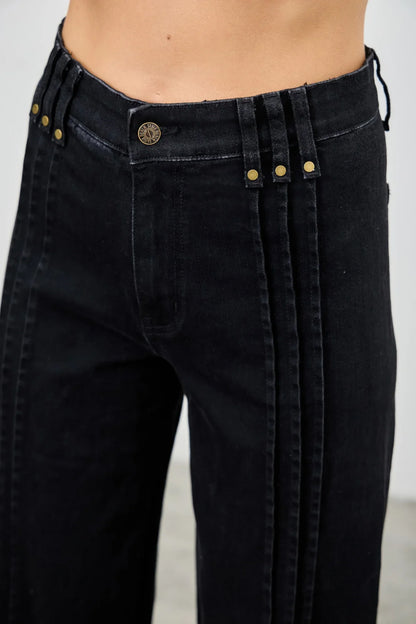 Close-up of high-waisted black denim pants with gold button details and wide belt loops