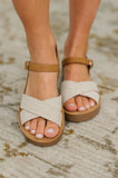 Close-up of cream nubuck wedge sandals with crisscross straps and ankle buckle on feet