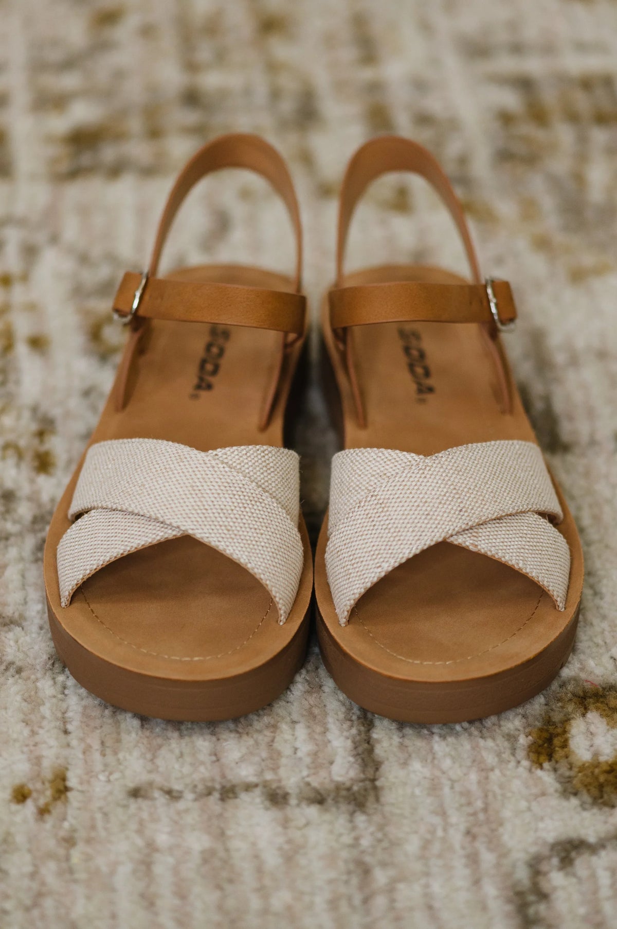Cream nubuck wedge sandals with tan ankle straps and crisscross canvas toes on textured rug