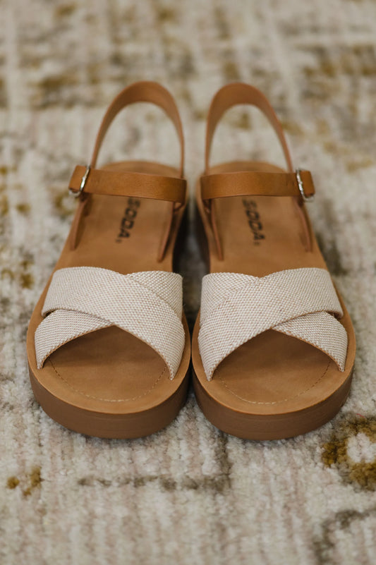 Cream nubuck wedge sandals with tan ankle straps and crisscross canvas toes on textured rug