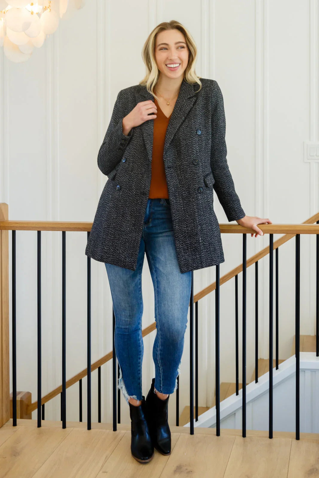 Woman wearing a black button-down blazer jacket with jeans and ankle boots indoors.