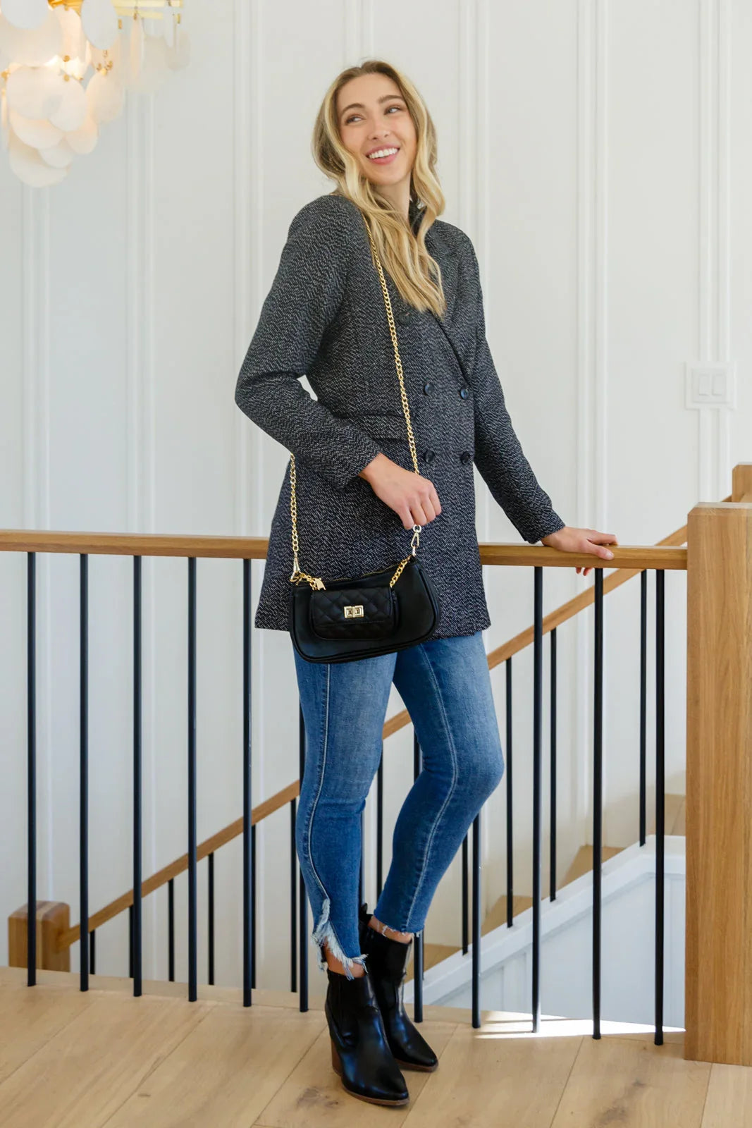 Woman wearing a black button-down blazer jacket, blue skinny jeans, and black ankle boots