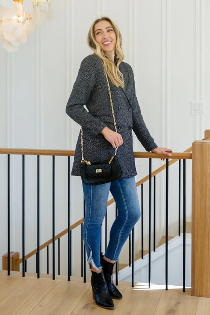 Woman wearing a black button-down blazer jacket, blue skinny jeans, and black ankle boots