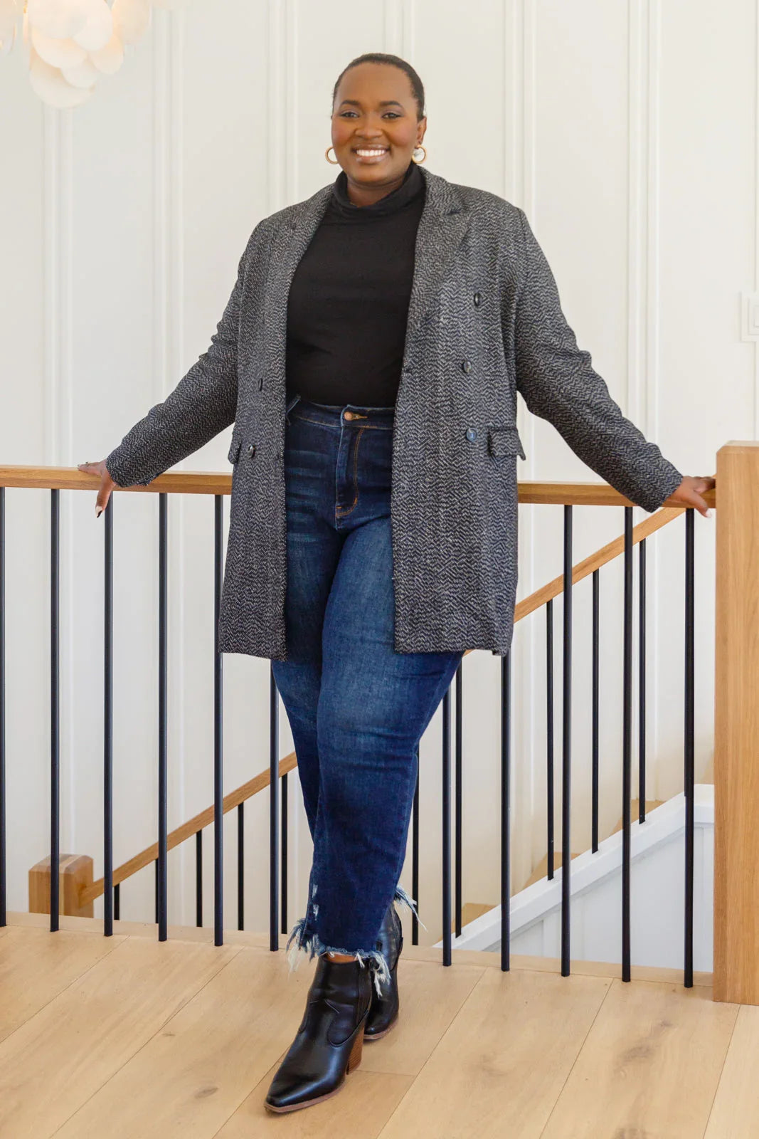 Woman wearing a black button-down blazer jacket, dark jeans, and ankle boots indoors
