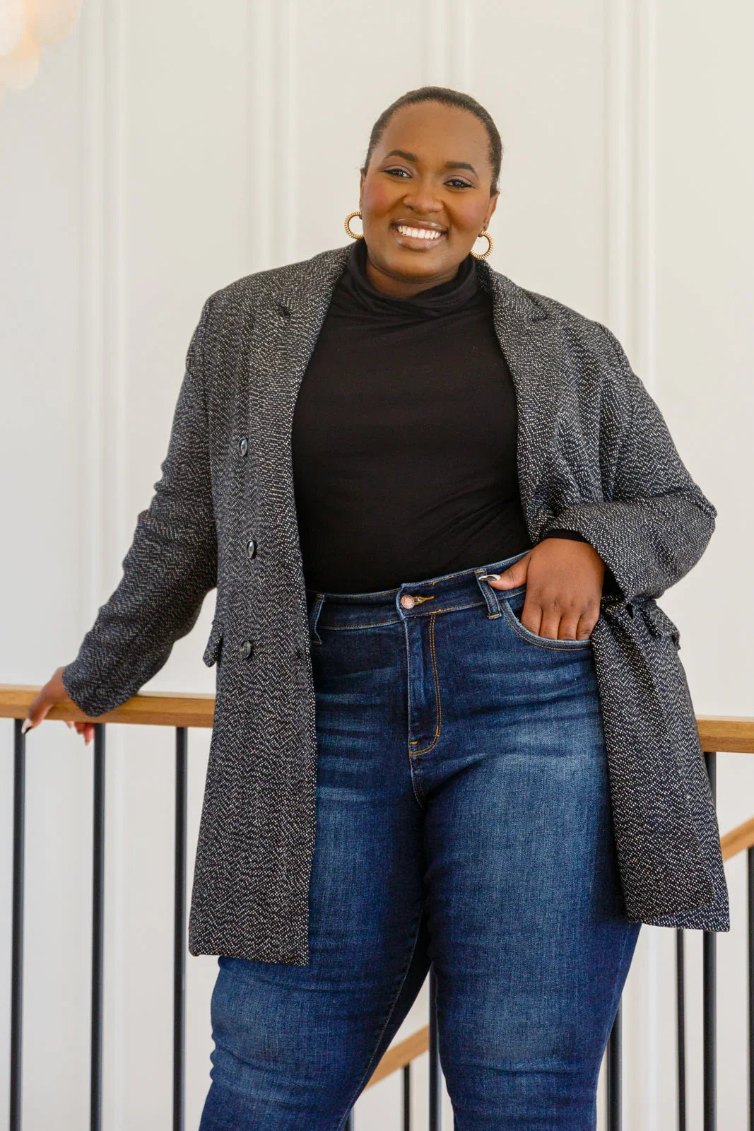 Woman wearing a black button-down blazer jacket, black top, and blue jeans indoors