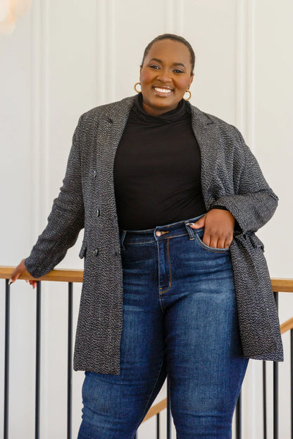Woman wearing a black button-down blazer jacket, black top, and blue jeans indoors