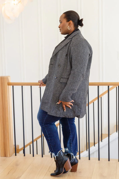 Woman wearing a textured black double-breasted blazer, blue jeans, and heeled boots indoors.