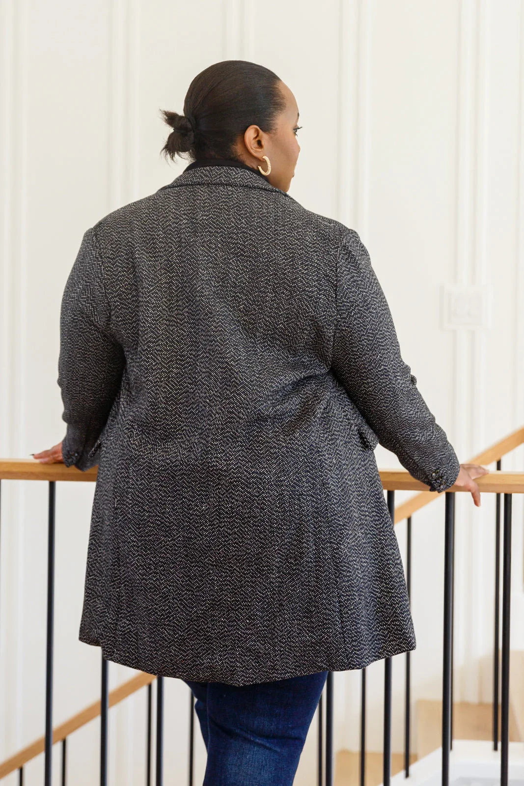 Woman wearing black patterned blazer jacket and dark jeans, shown from the back indoors