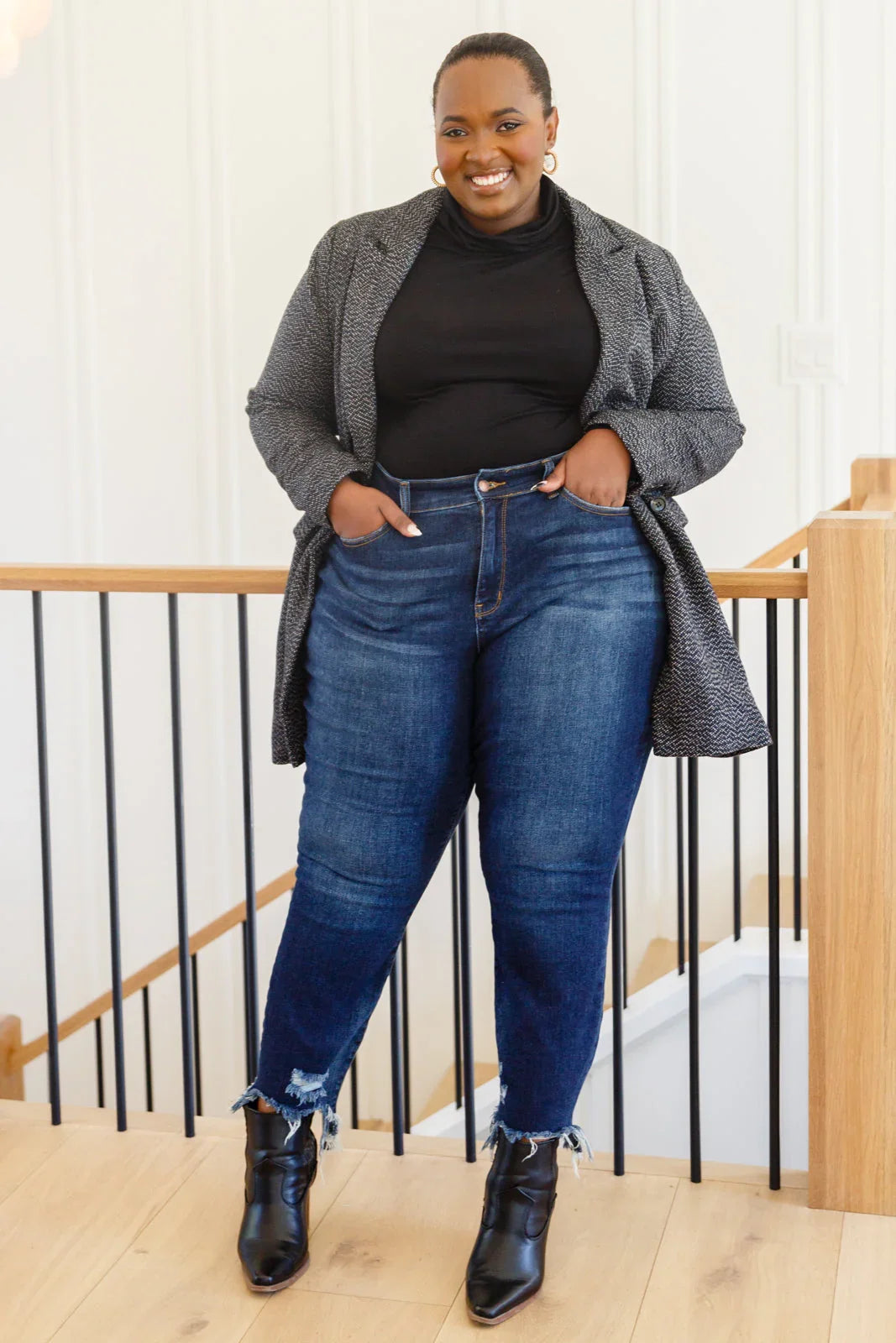 Woman wearing a black blazer, dark jeans, and black ankle boots standing indoors