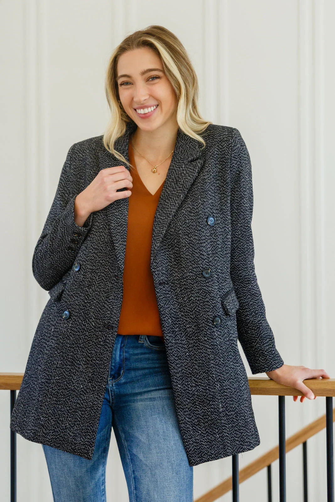 Woman wearing a black button-down blazer jacket with a brown top and blue jeans.