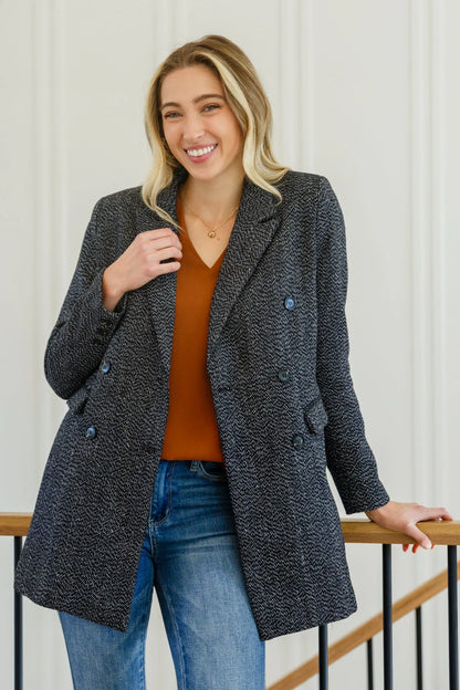 Woman wearing a black button-down blazer jacket with a brown top and blue jeans.