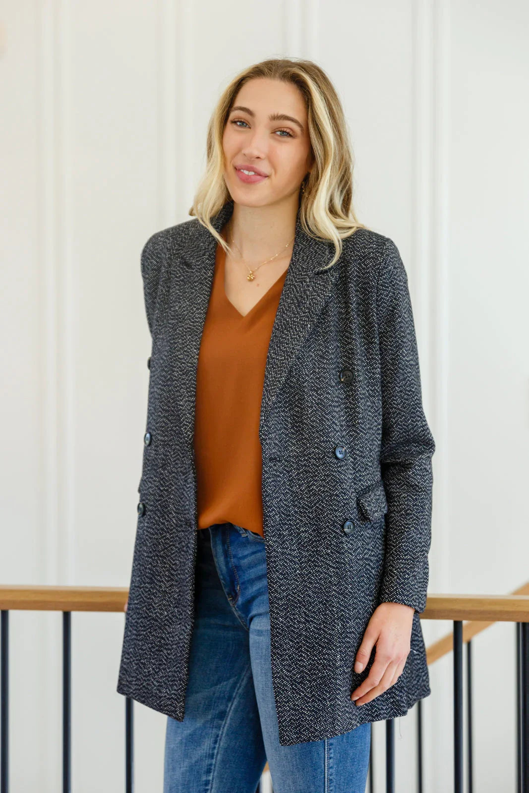 Woman wearing a black button-down blazer jacket with a brown top and blue jeans indoors.