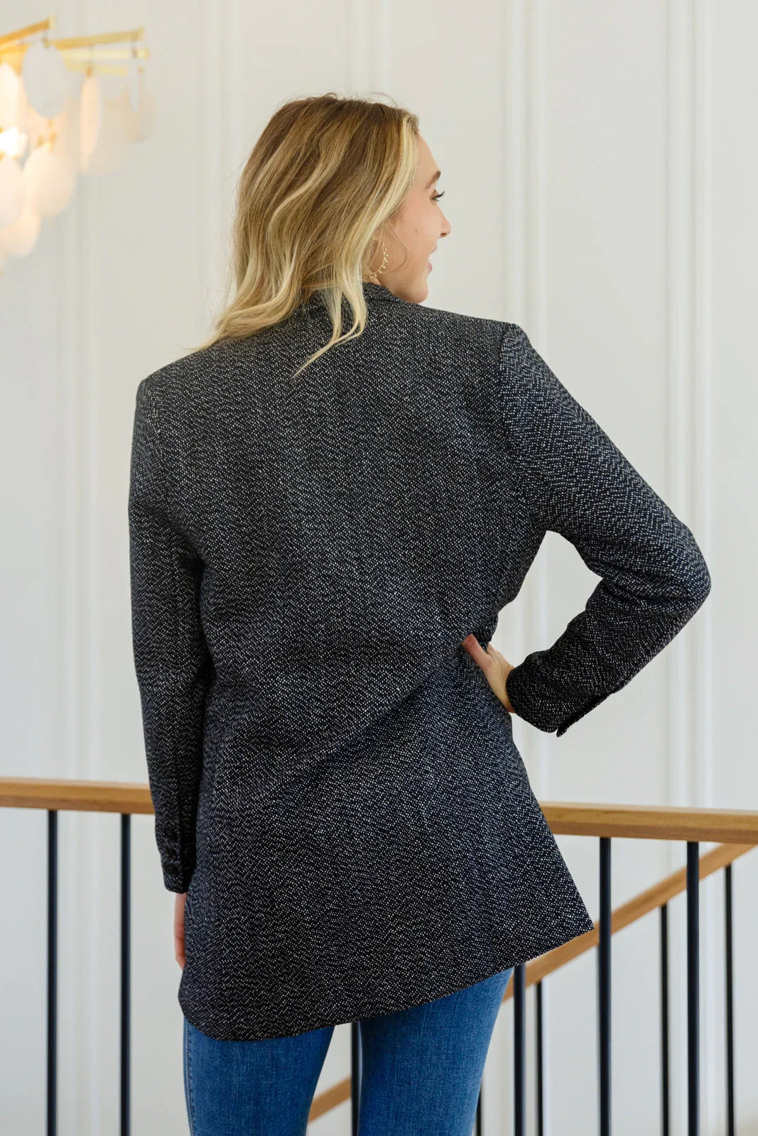 Woman wearing a textured black button-down blazer jacket with blue jeans, shown from the back.