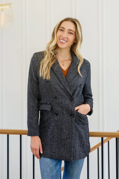 Woman wearing a black textured button-down blazer jacket and blue jeans indoors