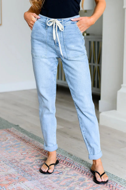 Woman in relaxed light wash high-waisted jeans with drawstring, black top, and sandals