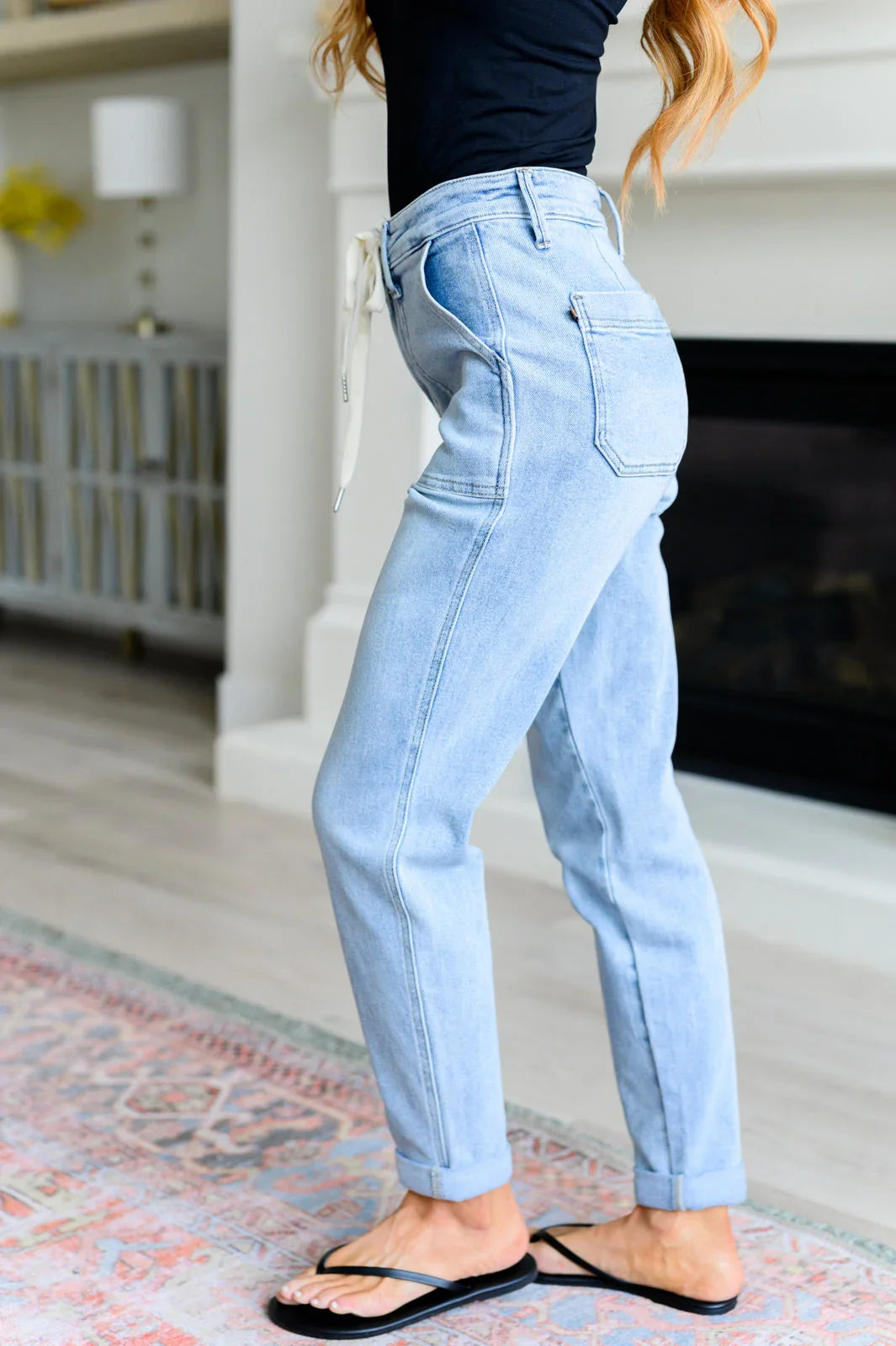 Woman wearing light wash high-waisted jeans with a drawstring, black top, and sandals indoors