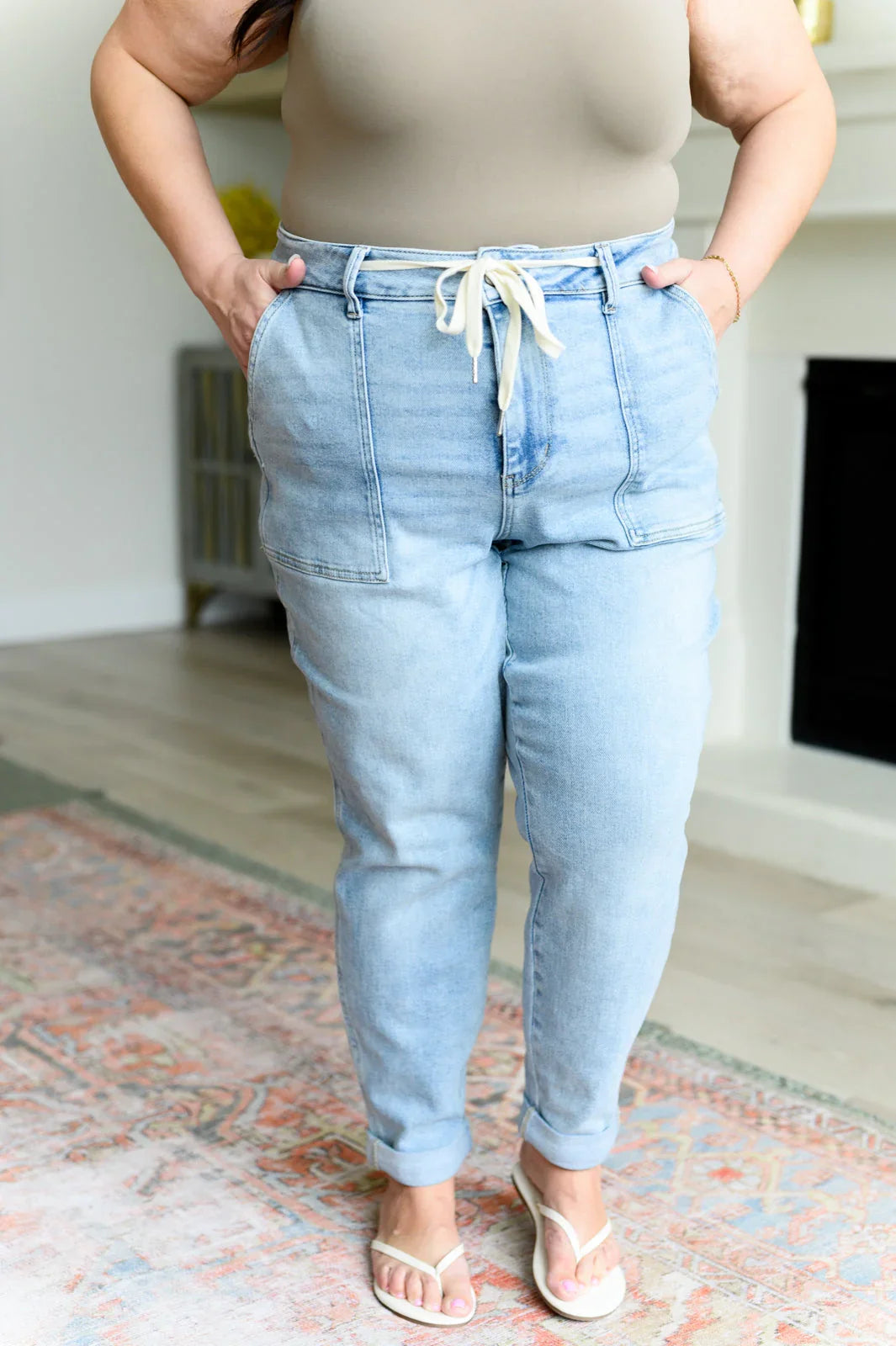 Woman wearing light wash drawstring denim pants with front pockets and white sandals indoors