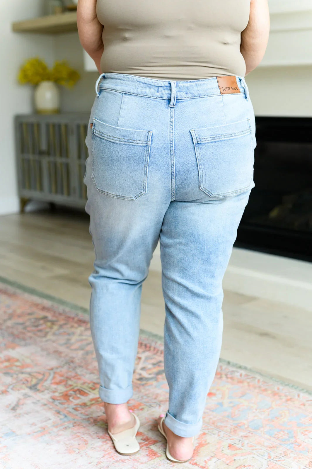Back view of woman in light wash high-waisted jeans and beige tank top, casual home setting