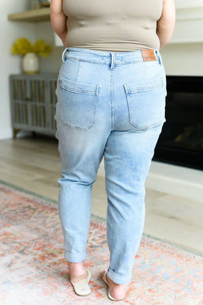 Back view of woman in light wash high-waisted jeans and beige tank top, casual home setting