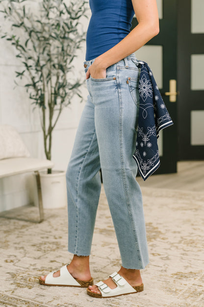 Person wearing blue jeans and white sandals with a blue bandana, standing in front of a door.