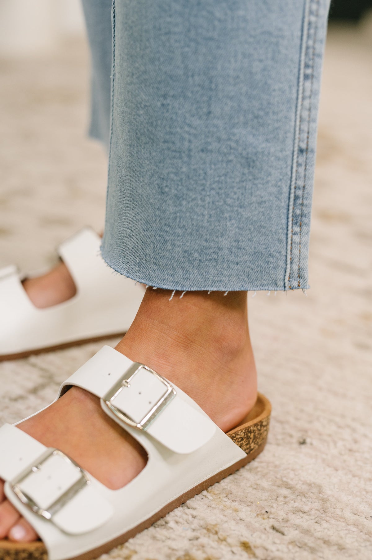 Close-up of a foot wearing a white sandal with a brown sole on a blurred background