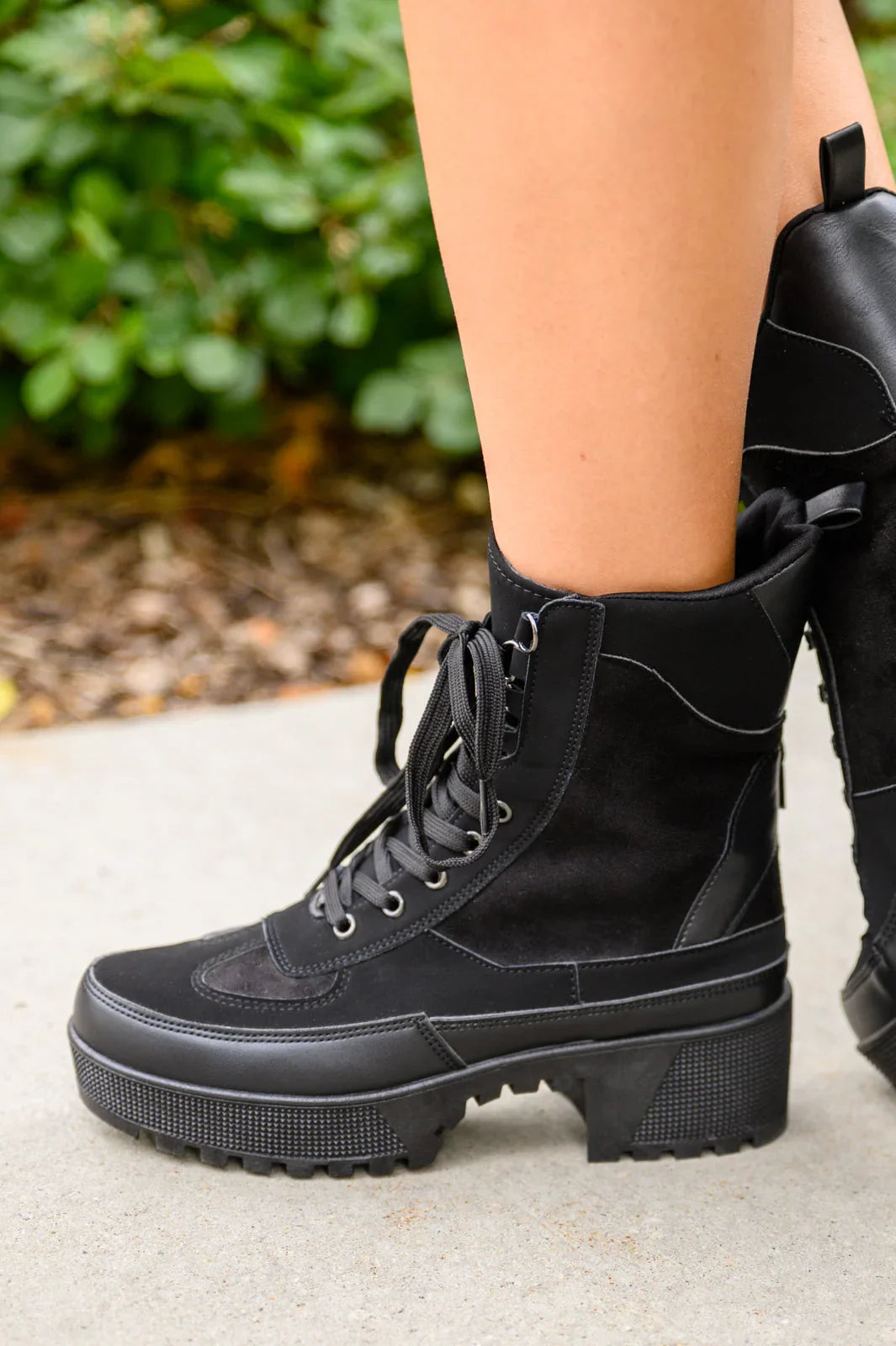 Black lace-up boots with chunky sole and suede panels worn outdoors on pavement