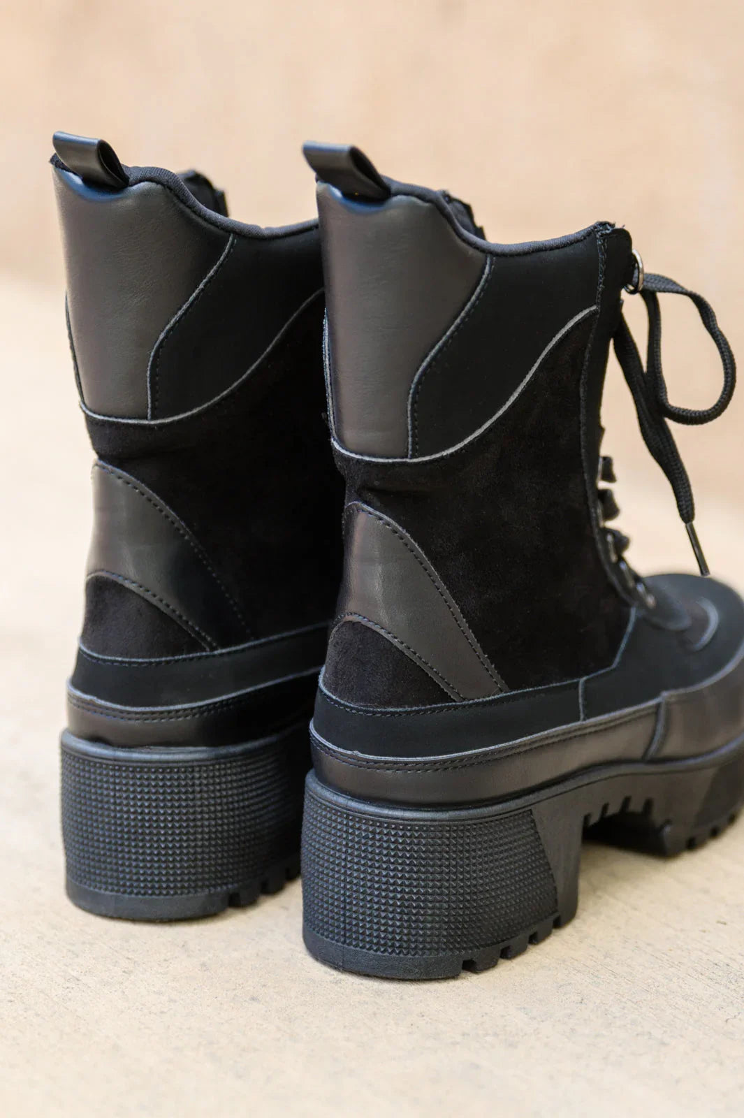 Close-up of black lace-up platform boots with chunky heels and mixed suede and leather texture.