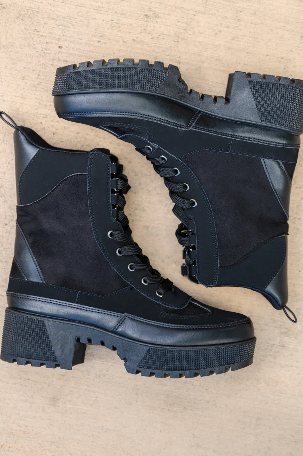 Black lace-up combat boots with chunky lug soles and suede panels on a neutral background.