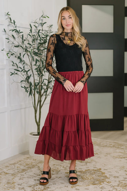 Woman wearing a burgundy tiered maxi skirt and black lace long sleeve top indoors