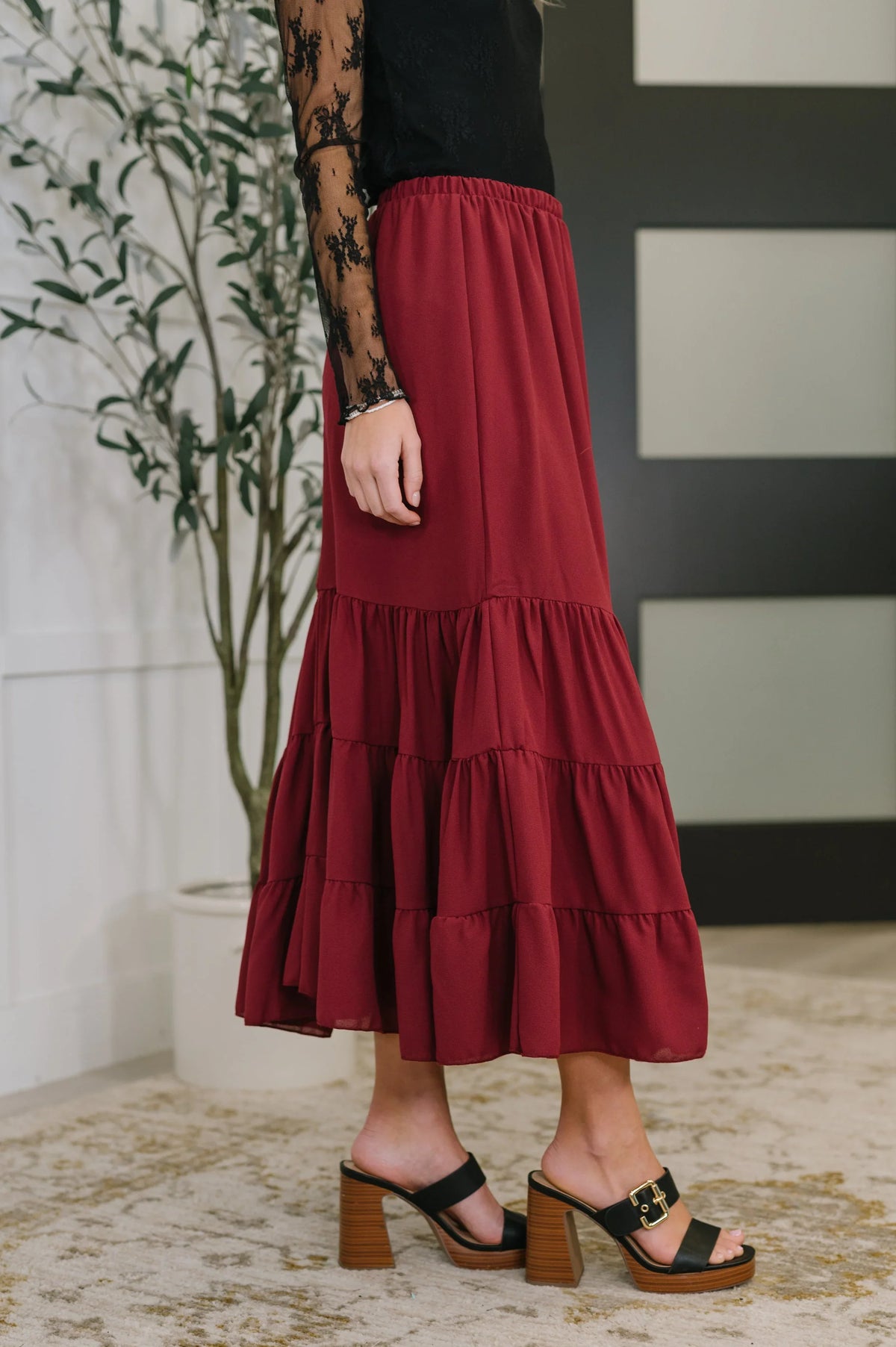 Woman wearing a tiered burgundy maxi skirt with black lace top and block heel sandals