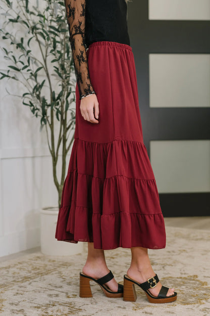 Woman wearing a tiered burgundy maxi skirt with black lace top and block heel sandals